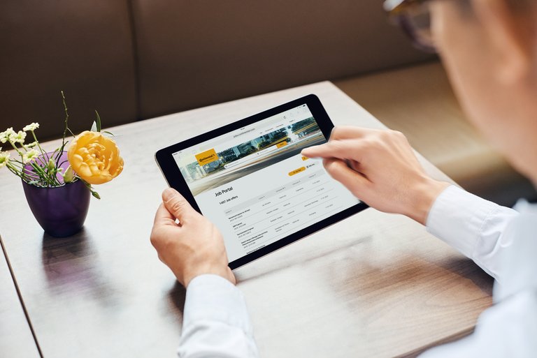 A person holding a tablet and looking for the right job on Continental’s job portal; on the table is a small bouquet of flowers