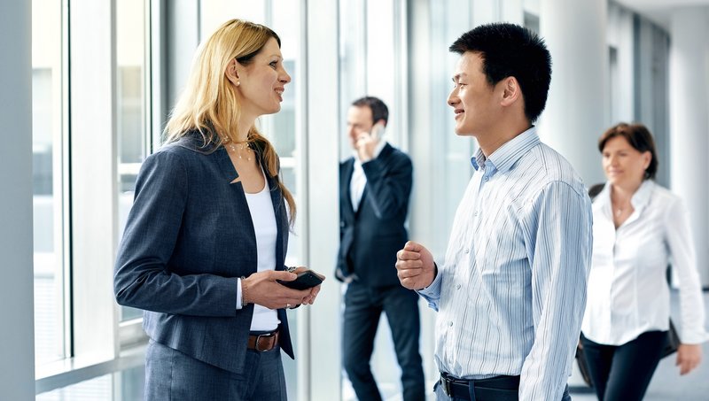 Two men and two women in business outfits walk smiling down a corridor