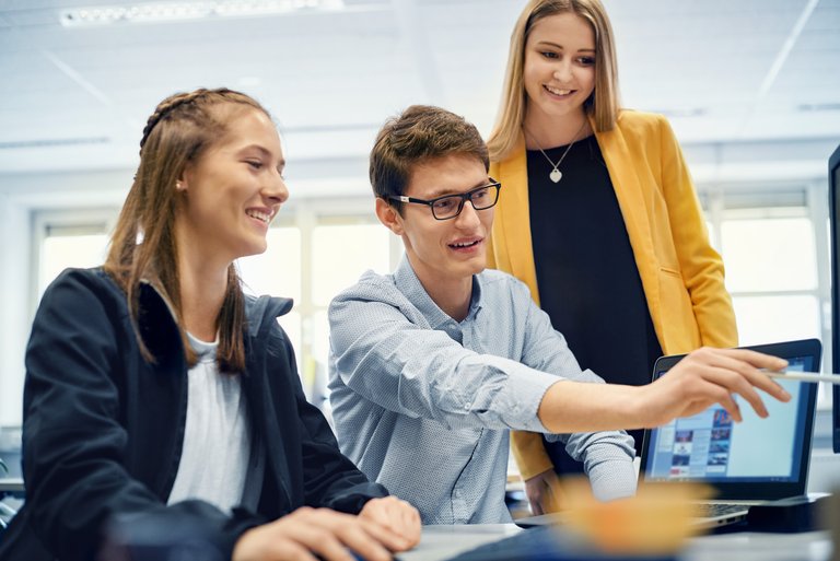 A young man with glasses shows two young women something on his PC
