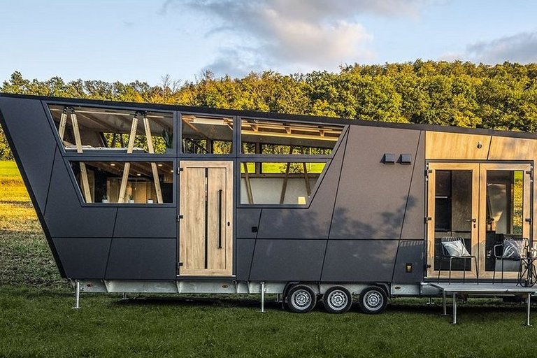 A futuristic tiny house stands on a meadow in front of a forest embankment