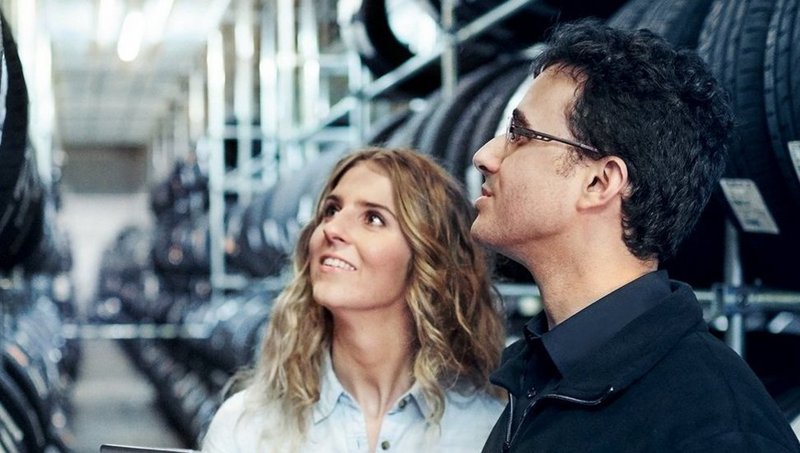 A young woman and a man look at a large rack of tyres