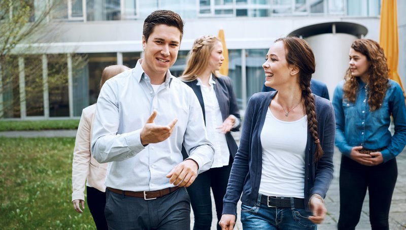 A group of young people walk smiling through a building courtyard